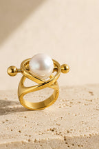 Atrani Orbit Ring standing on warm travertine stone, white pearl held inside crossing gold arcs
