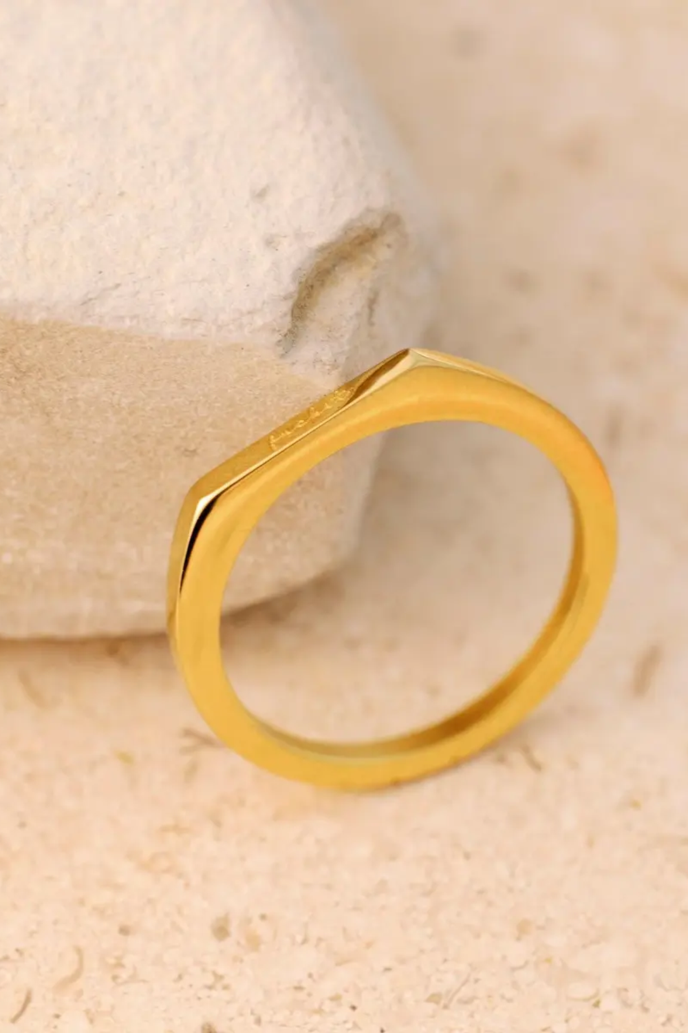 Basta Band gold engraved ring resting on travertine stone
