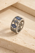 Cetara Evil Eye Ring on warm travertine stone, carved eye and hamsa band set with blue crystals