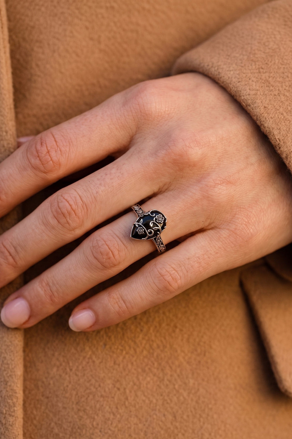 Ombra obsidian flower ring on a hand resting on a camel coat